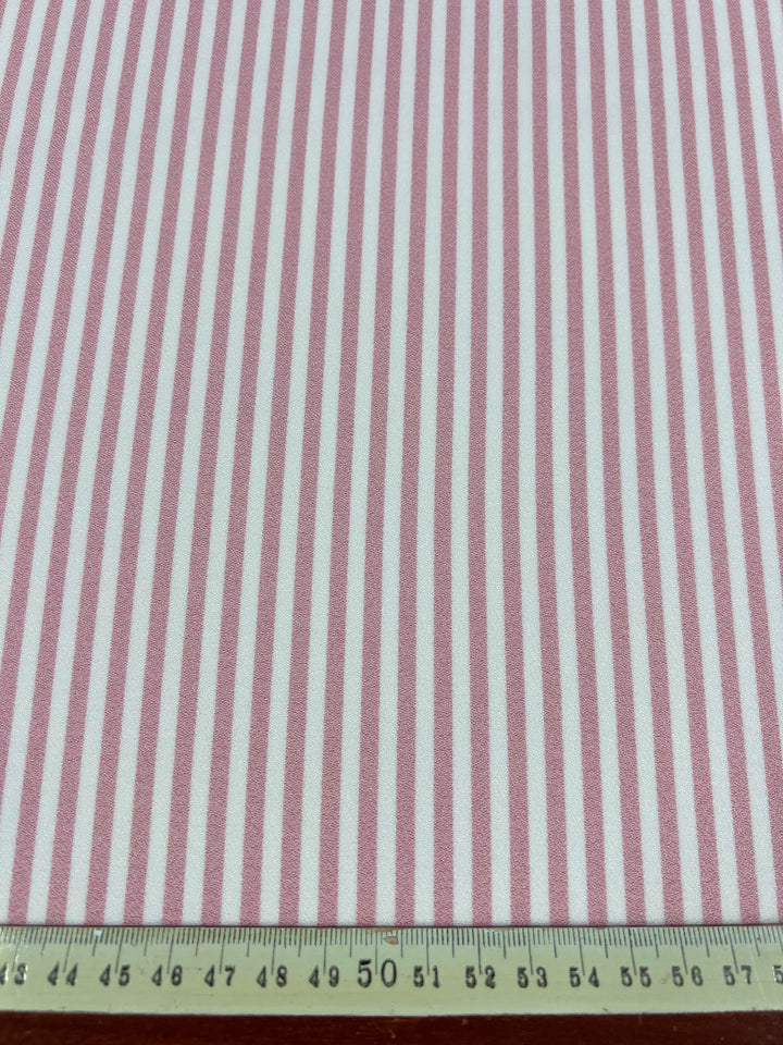 The Striped Crepe - Tickled Pink fabric by Super Cheap Fabrics features a fashionable design with vertical pink and white stripes on a high-quality polyester material. A centimeter measuring ruler is displayed at the bottom to show its dimensions.