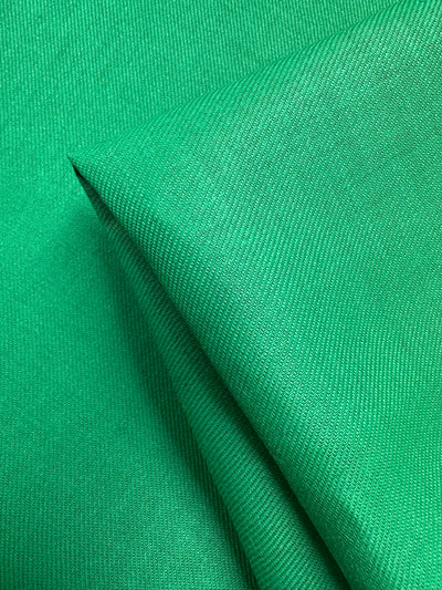 A close-up of Pure Washed Linen - Jelly Bean (140cm) by Super Cheap Fabrics shows one flat and another folded piece, highlighting its smooth texture and subtle weave—perfect for garment making.