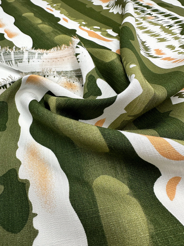 A close-up of Super Cheap Fabrics’ Bamboo Rayon - Torn Camo (150cm) features green, white, and orange abstract patterns with frayed edges, highlighting its lightweight texture—ideal for beginner sewing projects.