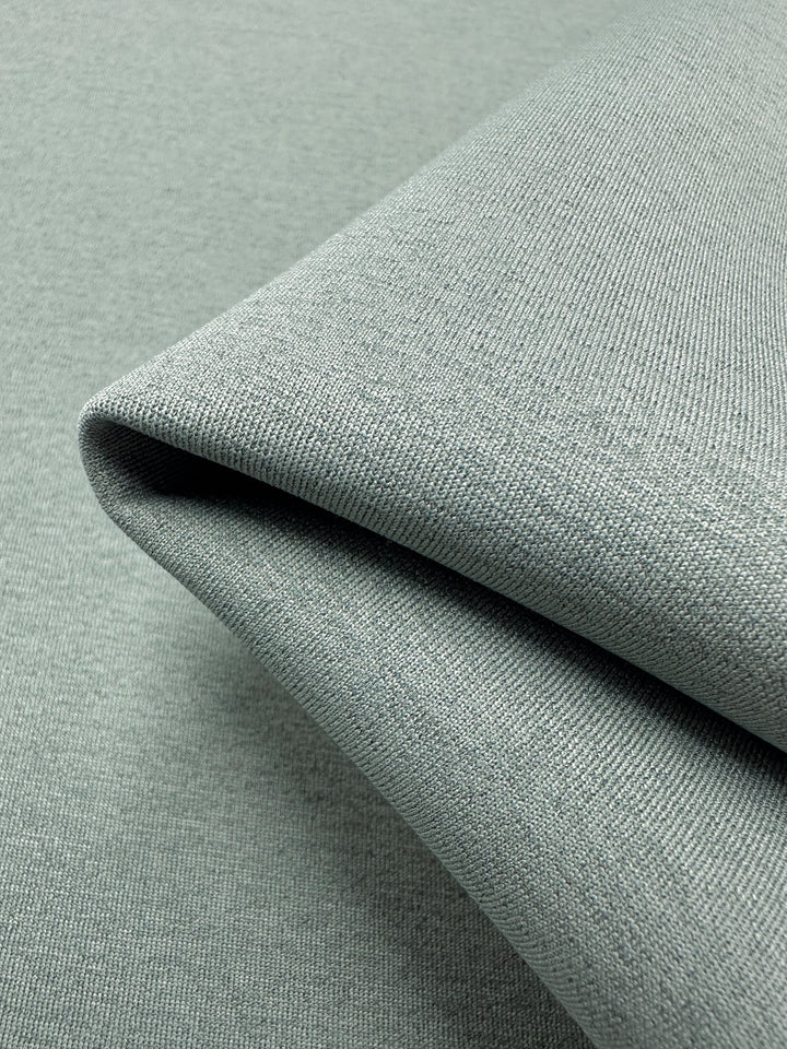 Close-up of neatly folded, light gray Scuba Knit - Mermaid - 165cm by Super Cheap Fabrics with a fine, slightly textured weave. The fabric's surface appears smooth and uniform, reflecting a soft sheen under the lighting.