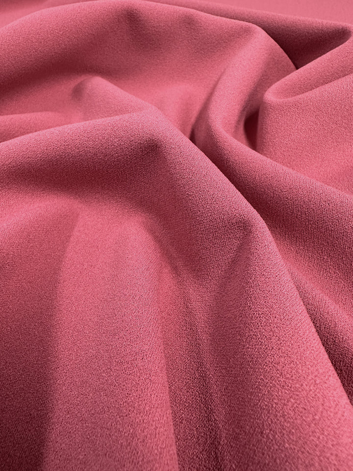 A close-up of Super Cheap Fabrics' "Plain Scuba Crepe - Holly Berry - 150cm" reveals a textured, crinkled surface. Light and shadows highlight its soft, undulating folds, characteristic of medium-weight fabric.