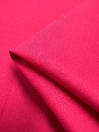 A close-up of Super Cheap Fabrics' Plain Sateen in Rose Red displays its smooth texture and layered folds. The 140cm fabric shimmers as it catches the light, accentuating its sheen and soft surface.