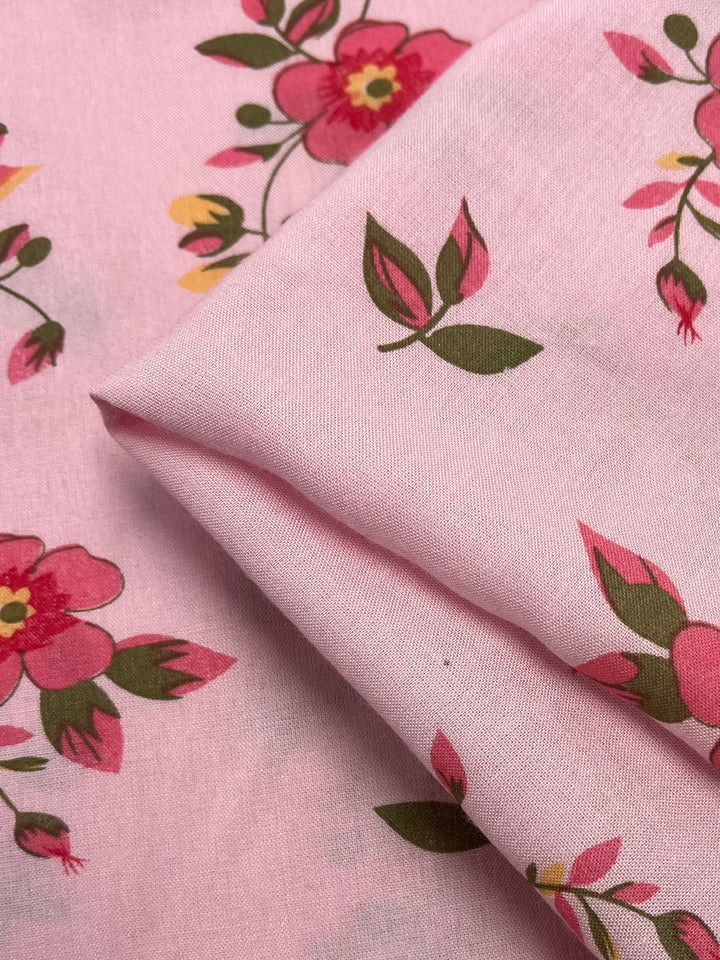 Close-up of Super Cheap Fabrics' 'Printed Rayon - Hippy Dais - 145cm', featuring a floral pattern with red and pink flowers and green leaves. The soft, vibrant fabric is gently folded, highlighting its texture—ideal for fans of lively prints.