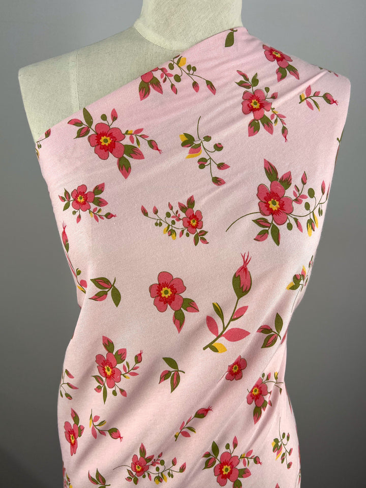 A close-up of a mannequin showcases Super Cheap Fabrics' Printed Rayon - Hippy Dais, featuring a lively floral design with red and pink flowers and green leaves on soft, versatile fabric.