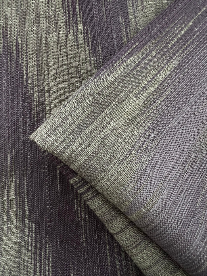 A close-up image of Upholstery Jacquard - Dusk - 145cm with a modern, abstract pattern. The fabric has a vertical streak design in shades of grey and light gold, creating a textured and dynamic appearance. Part of our affordable range from Super Cheap Fabrics, this durable stylish fabric is perfect for any interior project.