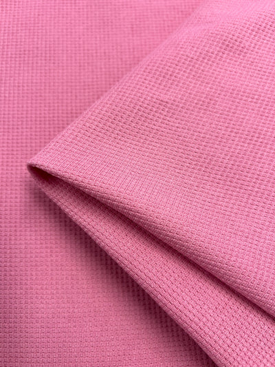 Close-up of a folded piece of Waffle Knit - Peony - 170cm by Super Cheap Fabrics with a subtle three-dimensional appearance. The material appears to be soft and slightly textured, showcasing the woven pattern in detail. The edge is neatly folded, highlighting the fabric's thickness and quality.