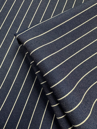 Close-up of two pieces of Chambray - Sargasso Sea (Super Cheap Fabrics), a navy cotton-nylon blend with white vertical pinstripes, one folded on the other. The fine weave and lightweight texture are clearly shown. Width: 150cm.