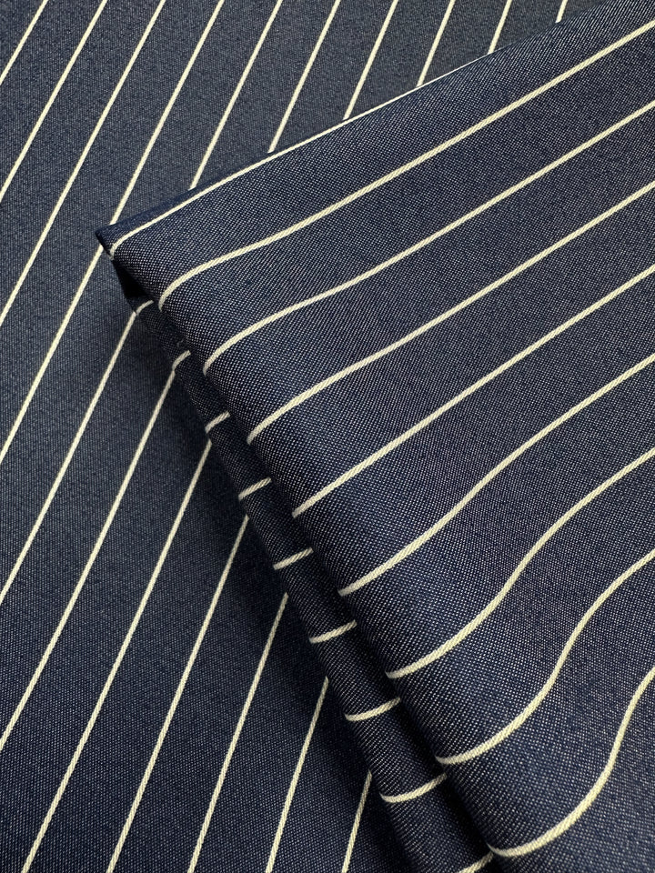 Close-up of two pieces of Chambray - Sargasso Sea (Super Cheap Fabrics), a navy cotton-nylon blend with white vertical pinstripes, one folded on the other. The fine weave and lightweight texture are clearly shown. Width: 150cm.