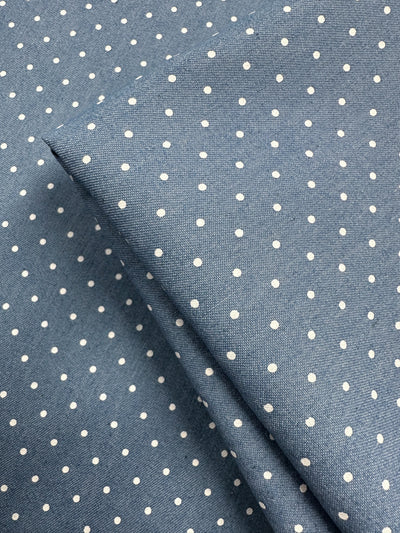 Close-up of Chambray - Blissful Spot (150cm) by Super Cheap Fabrics, featuring lightweight blue chambray with a white polka dot pattern and a folded section at the center.