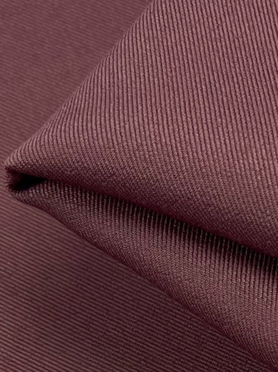 Close-up of folded mellow mauve fabric from Super Cheap Fabrics with a ribbed texture. The Twill Suiting, made from 100% polyester, features a diagonal weave pattern. The fold creates a slight shadow, emphasizing the rich texture and vibrant color.