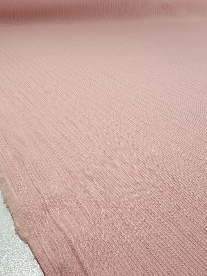 A close-up of Super Cheap Fabrics' Textured Cotton - Gossamer Pink (138cm) shows its soft, light pink ribbed material and detailed pattern spread on a flat surface.