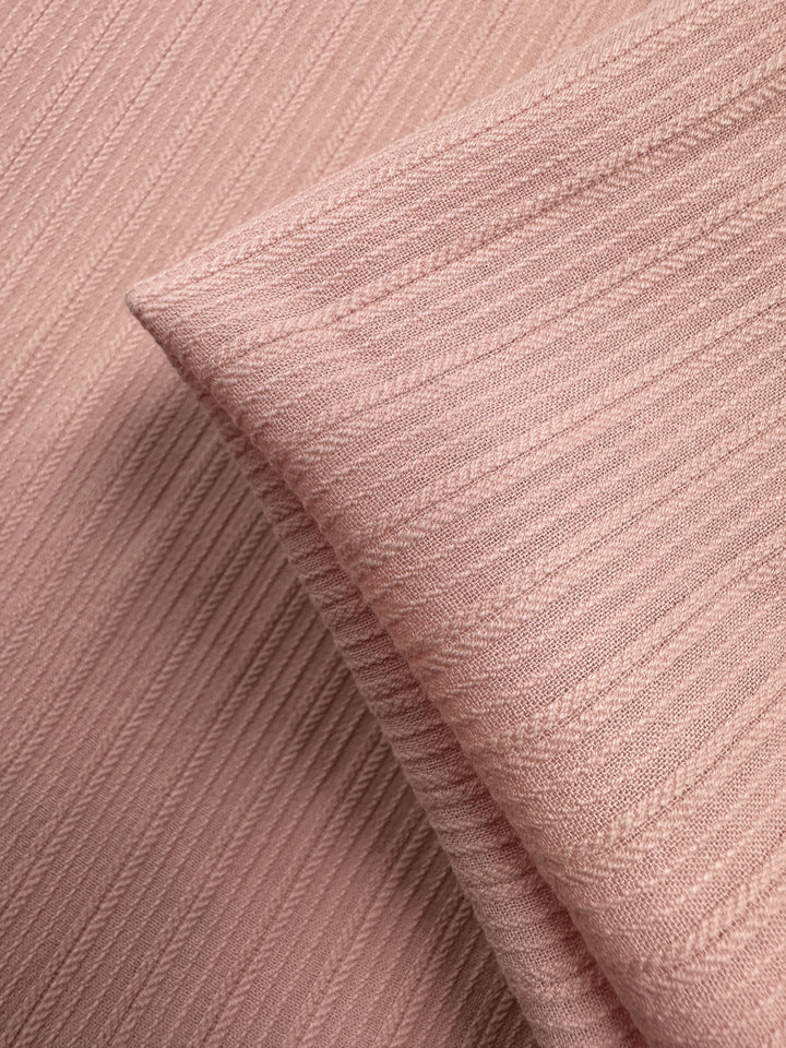 Close-up of Super Cheap Fabrics' Textured Cotton in Gossamer Pink (138cm), featuring soft, diagonally ribbed patterns and a neatly folded edge overlapping the background.