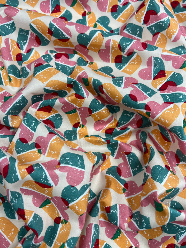 A close-up of a crumpled, printed cotton fabric featuring a colorful, heart-patterned design. The hearts are in shades of pink, green, yellow, and red, set against a white background made from natural cotton fibers. This multi-use fabric adds charm to any project. Introducing the "Printed Cotton - Fruity Candy Hearts - 148cm" by Super Cheap Fabrics.