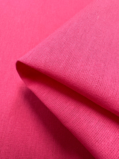 Close-up of Super Cheap Fabrics' Ramie Linen in Azalea Pink, 150cm wide. The natural ramie fiber's vibrant pink hue and detailed weave pattern stand out, with a neatly folded section creating a sharp crease.