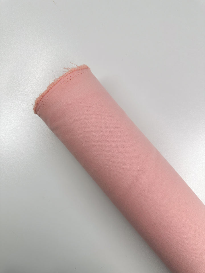 A roll of pale seashell pink fabric from Super Cheap Fabrics, made of natural Ramie Linen with a slightly frayed edge, rests against a white background.