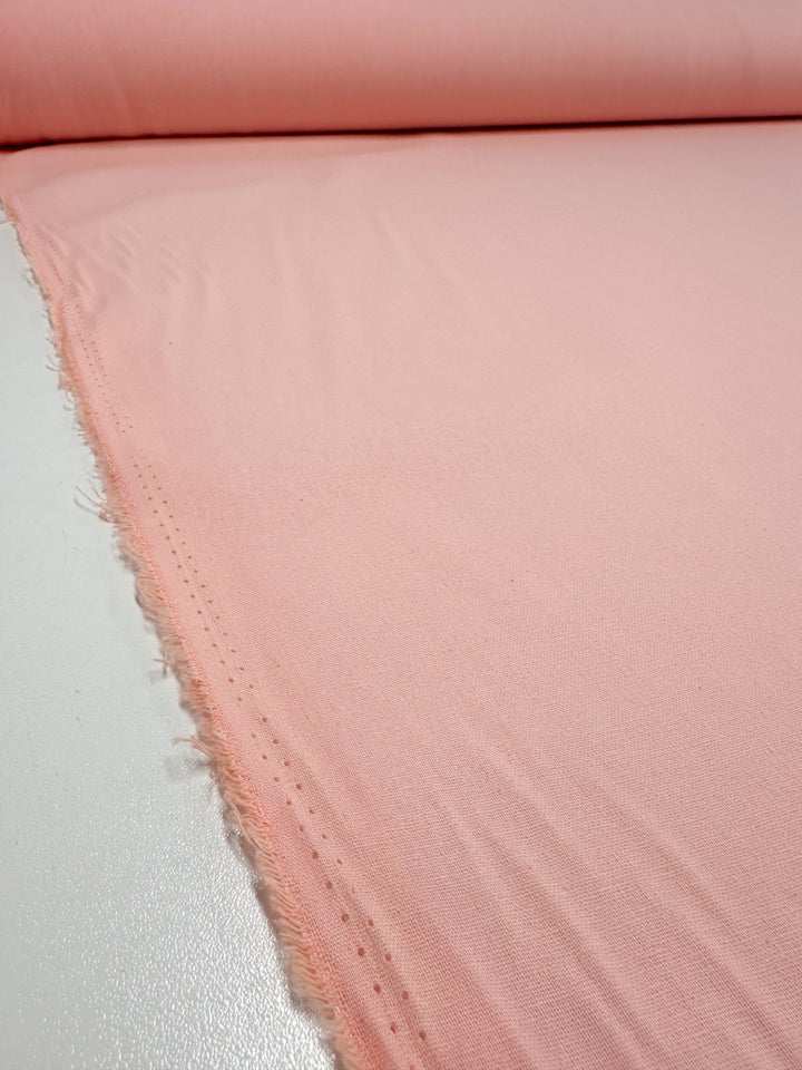 A close-up of Super Cheap Fabrics' Ramie Linen in Seashell Pink, 150cm wide, showcases its slightly frayed edge and smooth surface, highlighting the inviting texture and durability of this natural fiber.