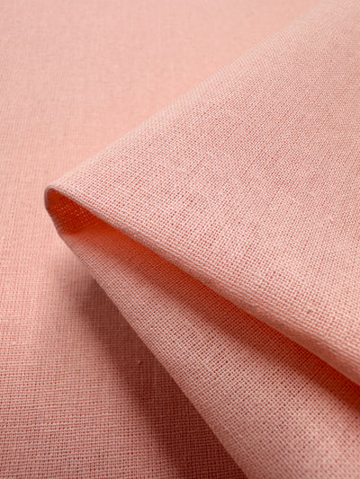 A close-up of a folded piece of Ramie Linen in Seashell Pink by Super Cheap Fabrics. This 150cm durable textile features a grid-like weave, adding visual depth, with the focus on the fold highlighting its natural fiber texture.