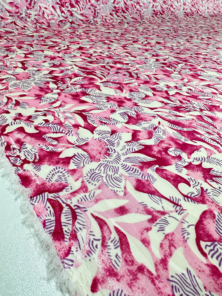 A close-up image of the "Silky Satin - Lotus - 150cm" by Super Cheap Fabrics shows a vibrant floral pattern with pink and white flowers on a light background, crafted from lightweight satin. The elegant piece is laid flat, highlighting intricate stylized petals and leaves.