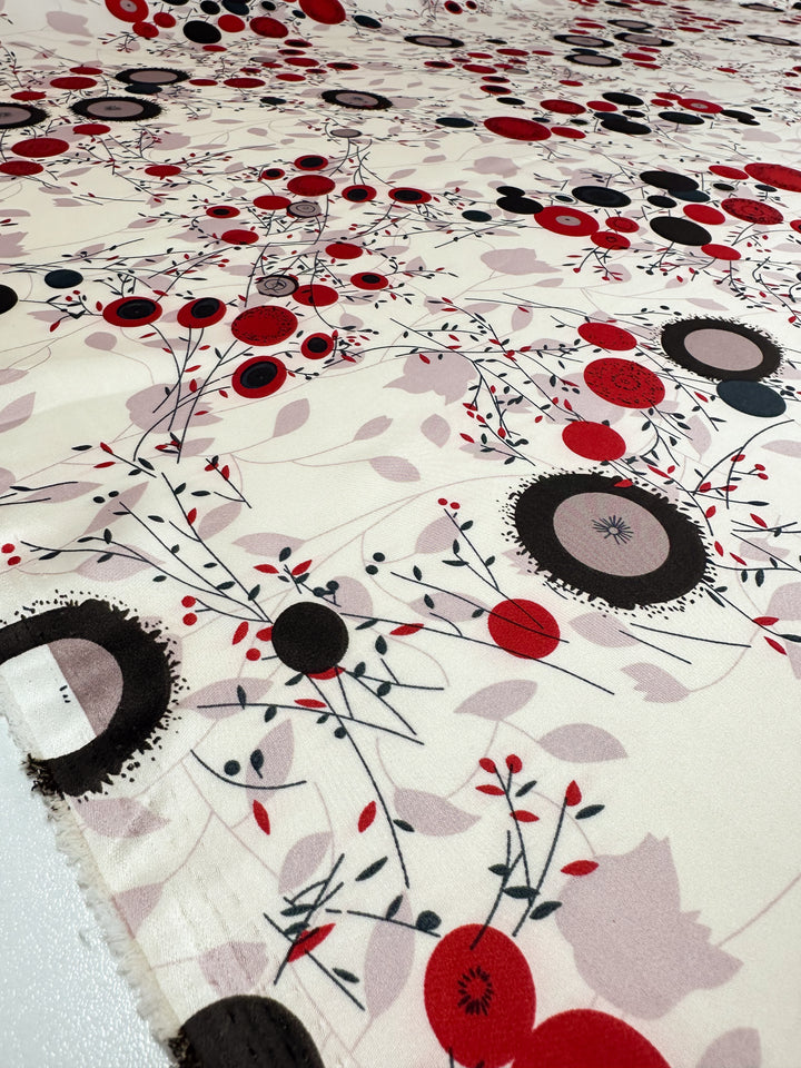 The Silky Satin - Dried Flower by Super Cheap Fabrics displays a stunning close-up of lightweight fabric with red, black, and grey abstract circles and floral designs against a white backdrop, embellished with intricate branches and leaves.