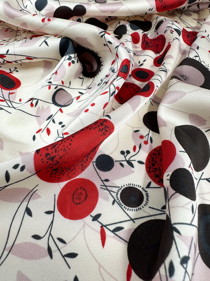 The Silky Satin - Dried Flower fabric by Super Cheap Fabrics features an elegant swirl of red, black, and gray florals with branches on a white background. It includes circular and leafy elements, highlighting the timeless beauty of lightweight printed satin. Width: 150cm.