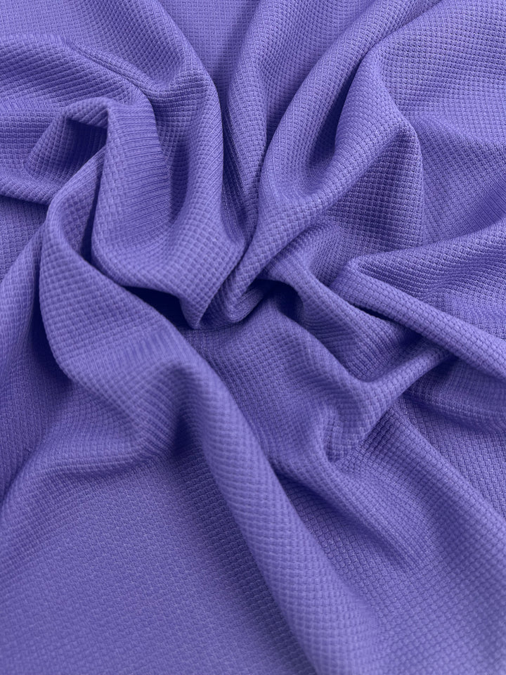 A close-up photo of a piece of crumpled Waffle Knit - Sunlit Allium from Super Cheap Fabrics. The material appears slightly textured with a small waffle pattern, creating a three-dimensional appearance and intricate design. The soft folds and creases enhance the fabric's tactile quality.