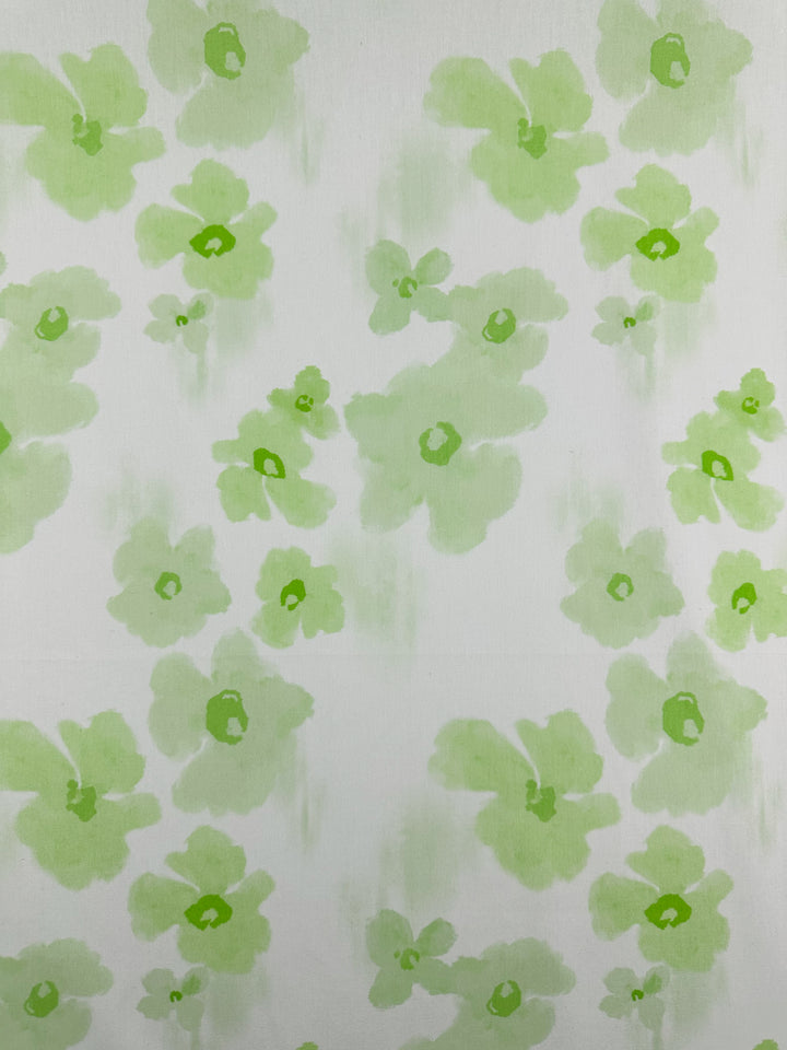 The "Lime Bloom" printed cotton by Super Cheap Fabrics showcases a soft and fresh aesthetic with light green watercolor flowers on a white background. Crafted from natural cotton fibers, each flower displays subtle shade variations, enhancing clothing and household items with depth and a delicate artistic touch at 150cm wide.