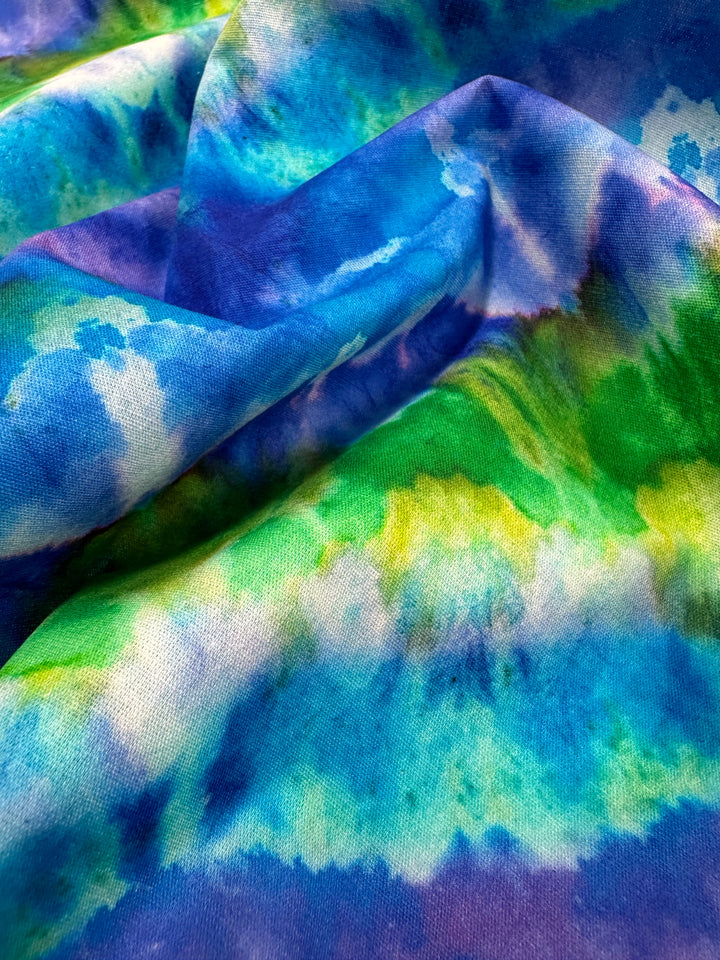 Close-up of the Printed Cotton - Lizard - 150cm from Super Cheap Fabrics, crafted with vibrant blue, green, and yellow hues. The colors blend and swirl to create a dynamic abstract pattern, while the texture of the natural cotton fibers adds depth to the design.