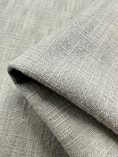 Close-up of a folded piece of Basket Dyed Cotton in Dove, highlighting its textured twill weave pattern. The fabric, by Super Cheap Fabrics, reveals a detailed structure and subtle tone variations typical of upholstery fabric.