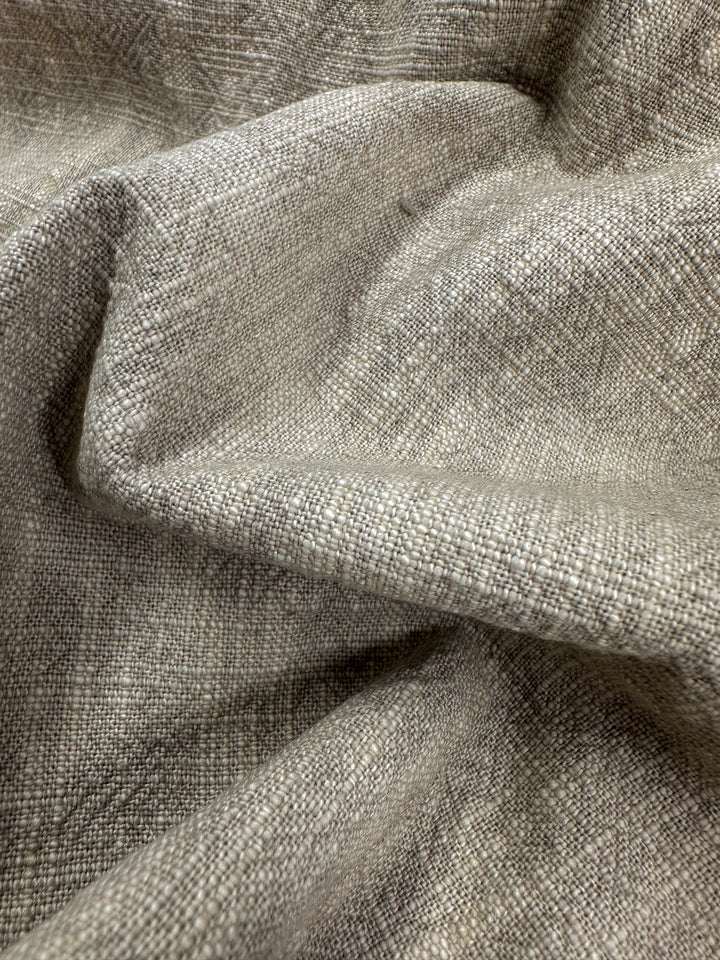 Close-up of textured taupe fabric with a visible twill weave pattern from Super Cheap Fabrics, creating gentle folds and shadows. The Basket Dyed Cotton material appears soft and slightly shiny, making it ideal for upholstery, suggesting a blend of natural or synthetic fibers.