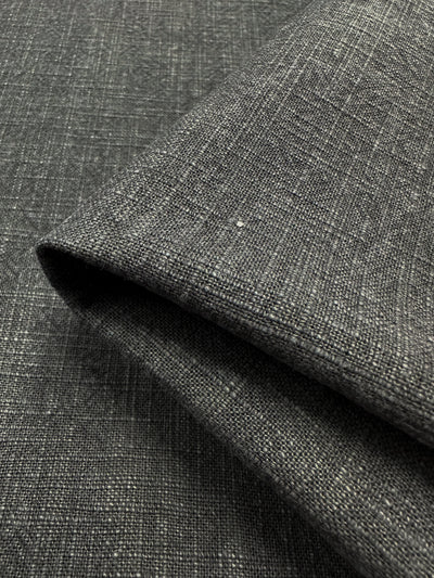 Close-up of the Basket Dyed Cotton in Charcoal from Super Cheap Fabrics, featuring 140cm wide dark gray textured upholstery fabric with a twill weave folded at the edge. The material showcases a woven pattern and subtle color variations, providing a sophisticated look.