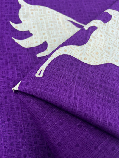 Textured, lightweight Bamboo Rayon in a vibrant purple color, patterned with a light cream design featuring stylized animal figures. The geometric shapes outline the animal, and the fabric appears folded in the foreground. Perfect for beginner-friendly projects. Available as "Bamboo Rayon - Lily Shadows - 152cm" from Super Cheap Fabrics.