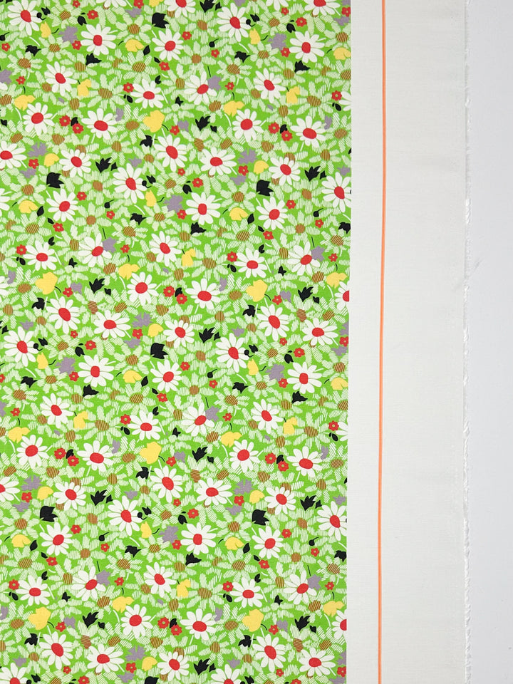 The Printed Linen - Daised by Super Cheap Fabrics features a green floral pattern with white daisies, red flowers, and lush green leaves. Ideal for garments or home decor, it includes a plain white strip with a thin orange line running vertically on the right side. Width: 138cm.