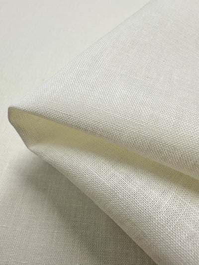 A folded piece of Pure Linen - Ivory - 138cm by Super Cheap Fabrics lies on a matching background, showcasing its lightweight weave that exudes both softness and durability.