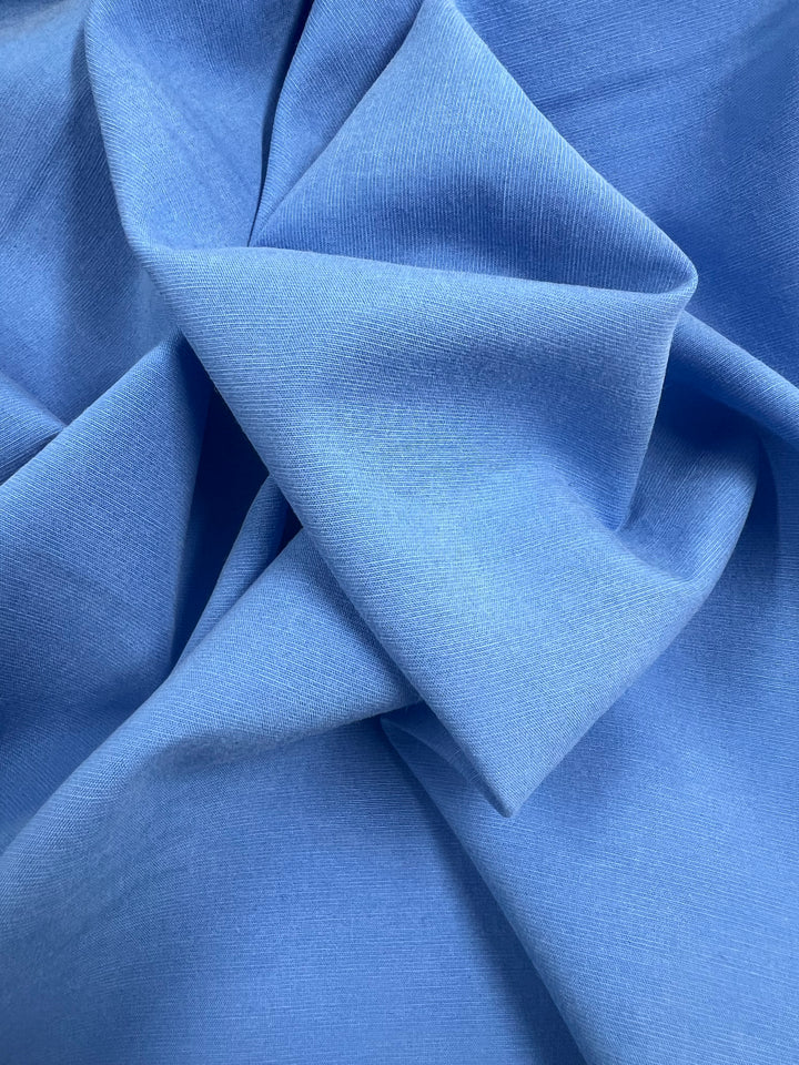 A close-up of the crumpled Silver Lake Blue twill suiting fabric from Super Cheap Fabrics showcases its soft texture with gentle folds. This 145cm wide, medium-weight suiting fabric features a smooth and slightly shiny surface, creating an intriguing play of light and shadow—ideal for those looking to add a touch of elegance with 100% cotton.