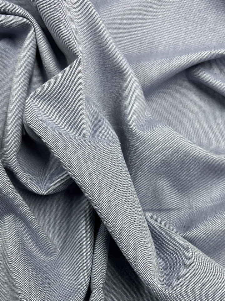 A close-up of the light gray Eventide suiting fabric from Super Cheap Fabrics showcases its intricate twill-like patterns and smooth drape, with soft curves and shadows revealing subtle hints of Silver Lake Blue. Fabric width is 135cm.