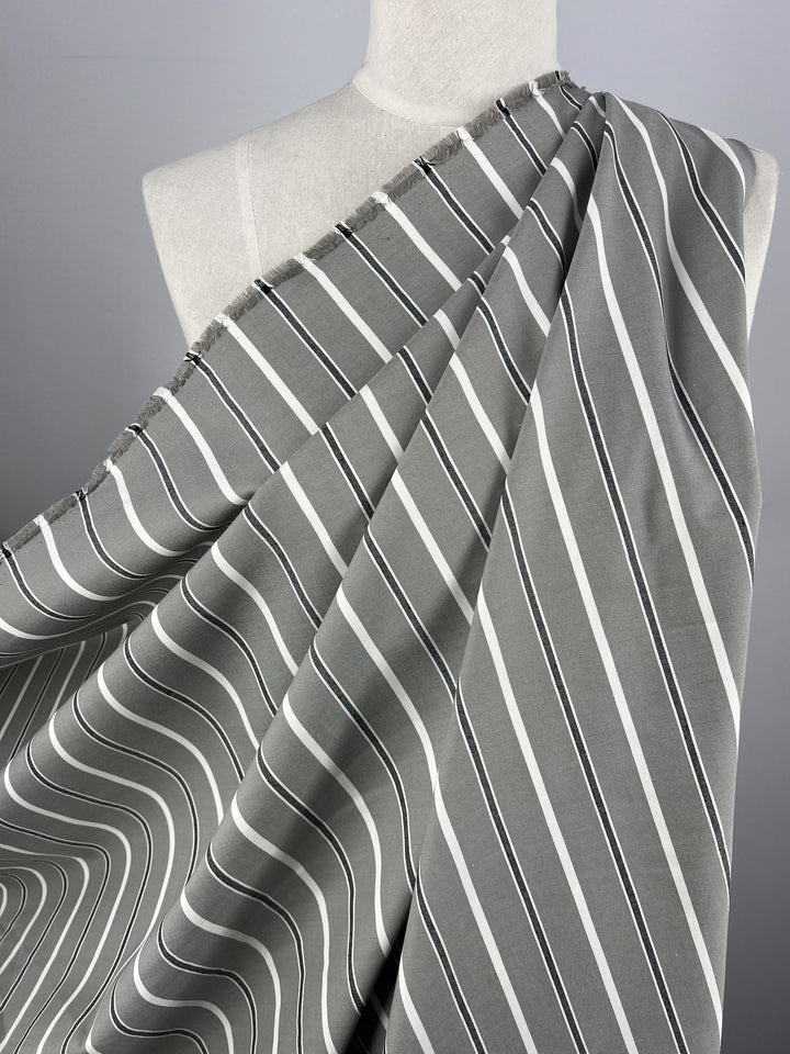 A mannequin is draped in Super Cheap Fabrics' Cotton Twill - Monochrome - 153cm, featuring lightweight cotton with white and black stripes. The dynamic visual pattern of curving and overlapping stripes covers one shoulder of the mannequin against a plain gradient background, evoking thoughts of stylish dresses or chic pants.