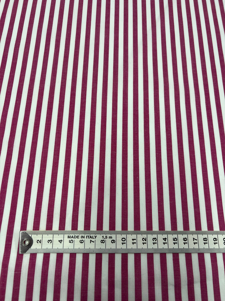 The Cotton Lawn - Lilac Rose from Super Cheap Fabrics, with its lightweight fabric featuring vertical pink and white stripes, is stretched out flat. Its silky finish highlights the texture. A tape measure at the bottom of this 100% cotton fabric, showing both metric and imperial units, marks "MADE IN ITALY.