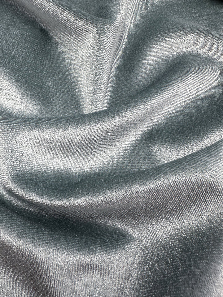 Close-up of Super Cheap Fabrics' Stretch Velour in High Rise, demonstrating its silver metallic sheen and smooth texture. The 170cm medium weight fabric is soft and reflective, with elegant folds enhancing depth, epitomizing modern textiles.