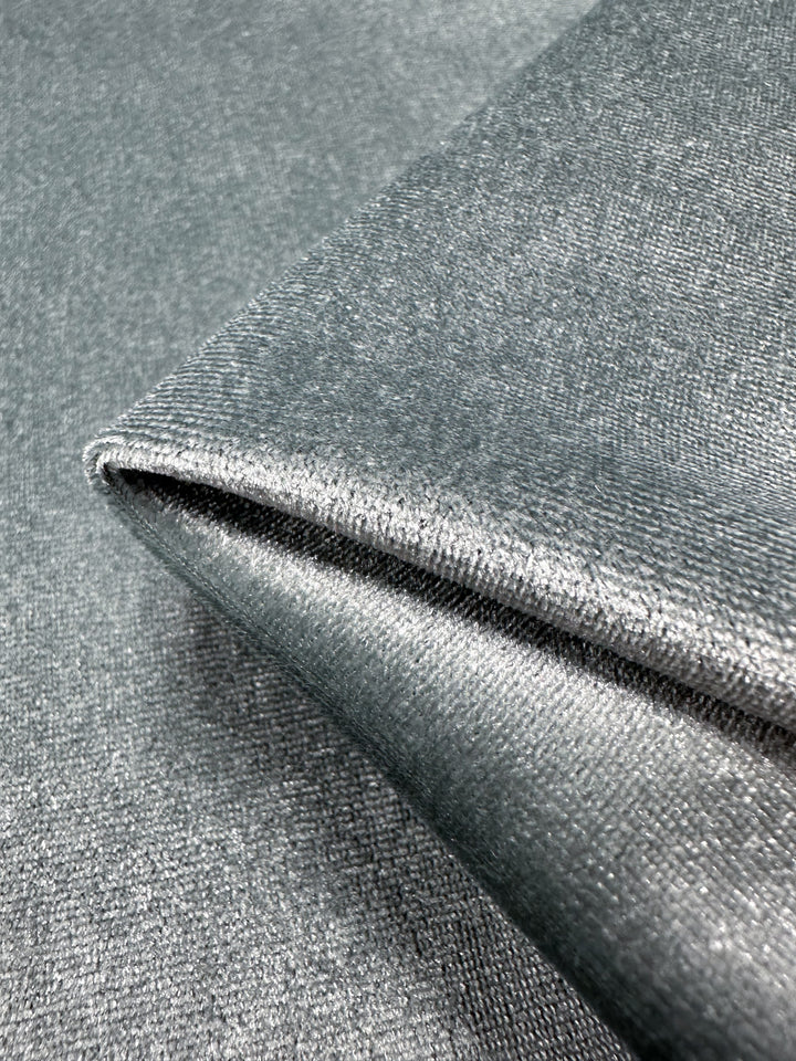 A close-up of Stretch Velour - High Rise by Super Cheap Fabrics reveals a folded piece of shiny, silver-gray fabric with a smooth texture, reflecting light to highlight its subtle sheen and fine threads typical of medium-weight stretch velour fabric.