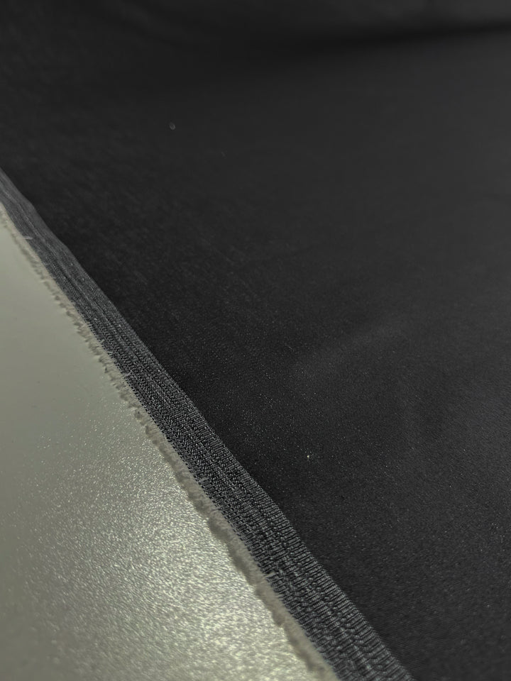 A close-up image of a sewing seam where Super Cheap Fabrics' Stretch Denim - Raven - 150 cm meets a gray surface, neatly stitched with cotton yarns, emphasizing the lightweight denim's texture and the contrasting colors.