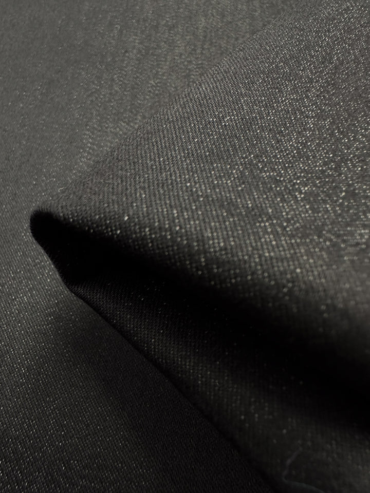 Close-up of Super Cheap Fabrics Stretch Denim - Raven - 150cm, a dark gray lightweight denim with a subtle textured pattern. Light plays on its smooth surface, highlighting the weave and folds that display its flexibility.