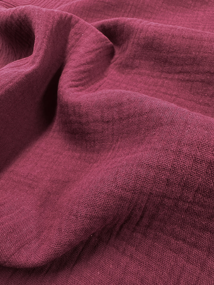 Close-up of the Muslin - Rumba Red from Super Cheap Fabrics, featuring a burgundy textured fabric with soft folds and subtle patterns. The organic texture of the 135cm fabric appears slightly wrinkled, highlighting its intricate weave and depth.