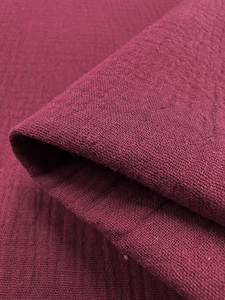 A detailed view of a rolled Muslin - Rumba Red fabric by Super Cheap Fabrics reveals its textured, slightly rough surface. The visible weave is neatly folded, highlighting the vibrant color and material characteristics comparable to organic muslin fabric.