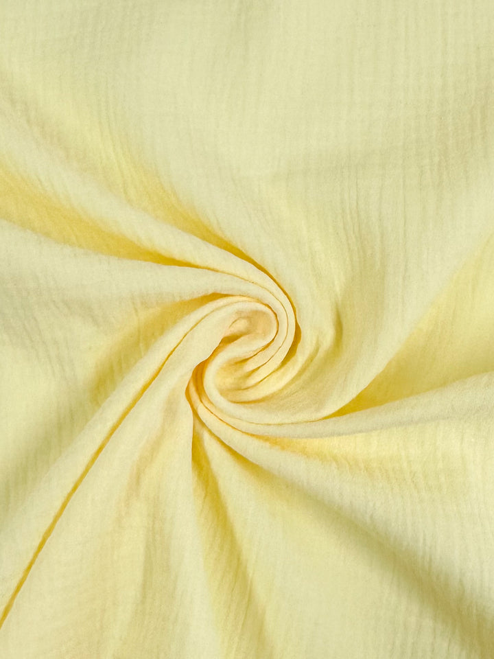 Zoomed-in view of Super Cheap Fabrics' Muslin in Pastel Yellow, measuring 135cm, featuring a central spiral fold pattern that forms a gentle swirl effect. The fabric's smooth yet slightly crinkled texture adds depth and embodies an elegant, reusable organic material.