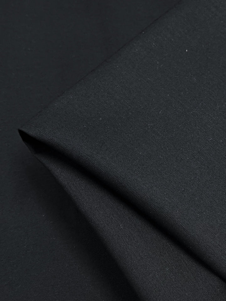 A close-up of folded navy Plain Sateen fabric, highlighting its smooth texture and precise creases by Super Cheap Fabrics.