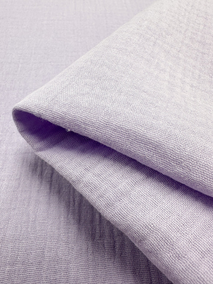 A detailed look at the Muslin - Lilac Breeze - 137cm from Super Cheap Fabrics, neatly folded to highlight its texture and weave. This organic fabric exudes softness and lightness, featuring a subtle grid pattern that makes it an attractive option for reusable cloths.