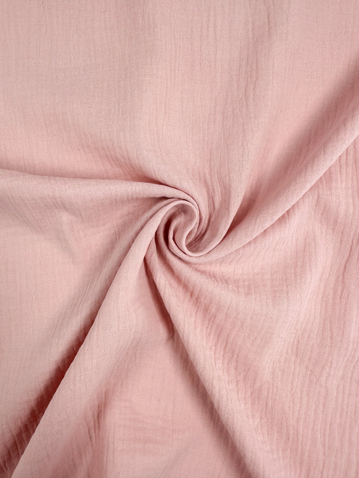 A detailed close-up showcases the soft, textured surface of the Super Cheap Fabrics' Muslin - Lotus - 135cm, skillfully twisted into a spiral pattern at the center.