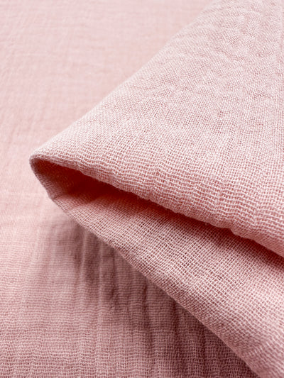 Close-up of Super Cheap Fabrics' Muslin in Lotus, measuring 135cm, showcasing its soft, textured pink organic fabric, neatly folded to highlight its woven pattern and gentle drape.