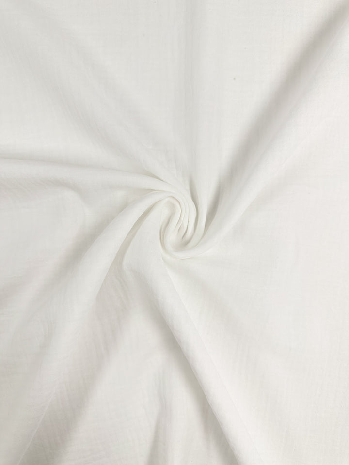 A close-up view of the Muslin - Ivory - 135cm by Super Cheap Fabrics reveals its organic texture and intricate spiral pattern. The reusable material feels soft and smooth, offering a delicate sheen.