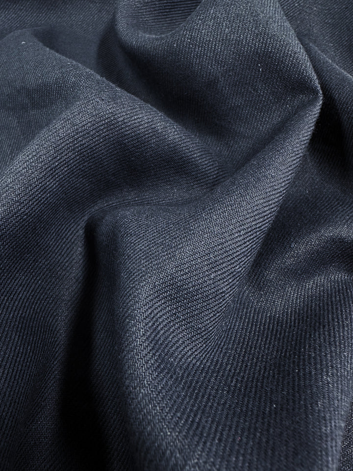 The Pure Washed Linen in India Ink by Super Cheap Fabrics features a close-up of its 140cm wide fabric. It has a subtle sheen, textured surface, gentle folds, and visible weave pattern, showcasing its soft and smooth quality ideal for garments.